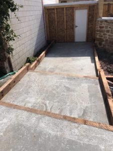 Construcción de base sólida para caseta de jardín utilizando traviesas de tren de madera tratada sobre suelo de hormigón.
