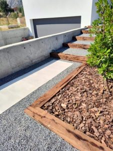 Escaleras de jardín construidas con traviesas de tren de madera rústica, rodeadas de grava decorativa y plantas.