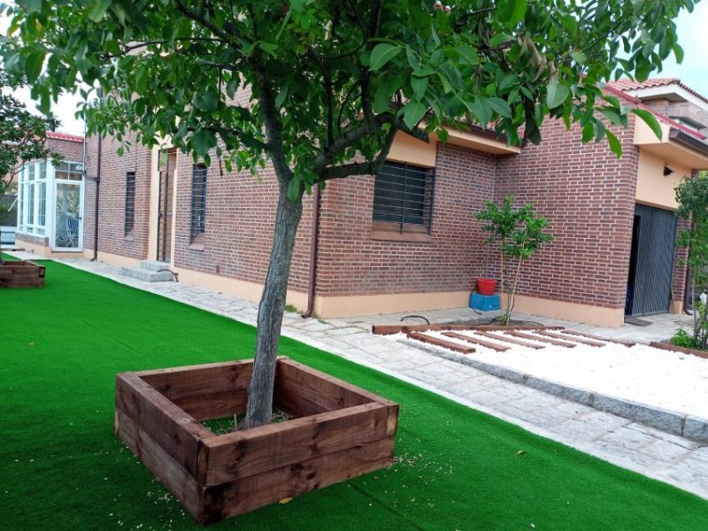 Jardinera de madera tipo alcorque fabricada con traviesas de tren para decorar la base de un árbol.
