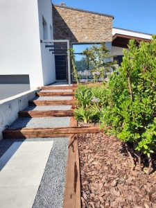 Detalle de estructura de vigas de madera tratada en fachada moderna combinada con muro de piedra rústica.