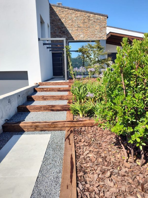 Detalle de estructura de vigas de madera tratada en fachada moderna combinada con muro de piedra rústica.