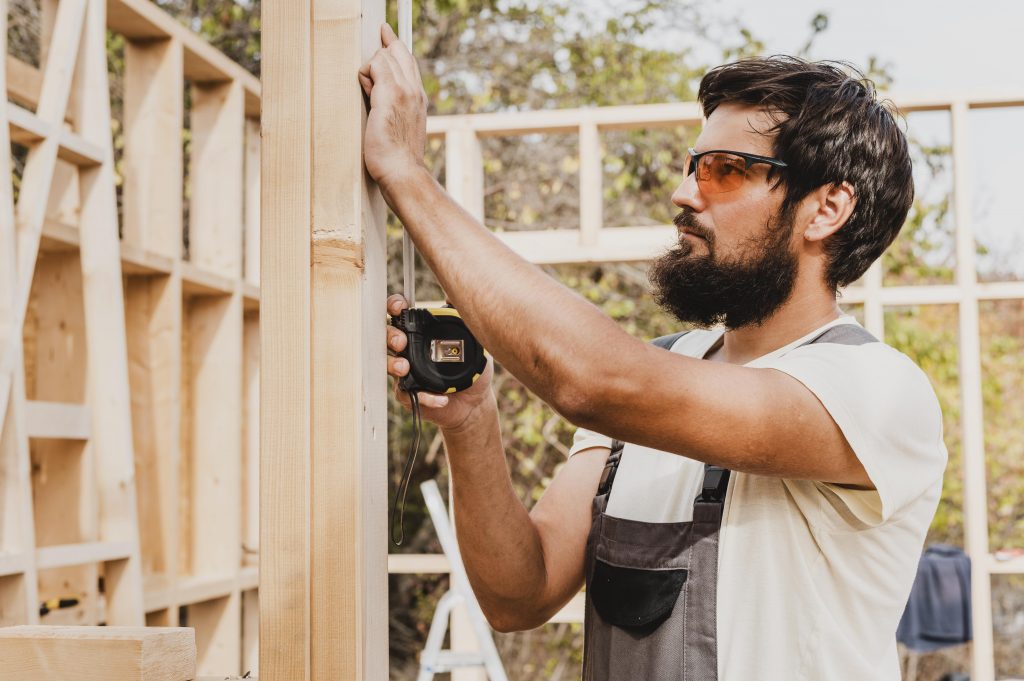 Carpintero profesional midiendo una estructura de madera para la instalación de traviesas de tren tratadas en un proyecto de exterior.