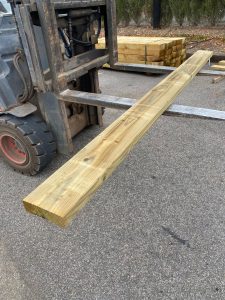 Carretilla elevadora industrial transportando una traviesa de madera recuperada tono miel para jardines y paisajismo.